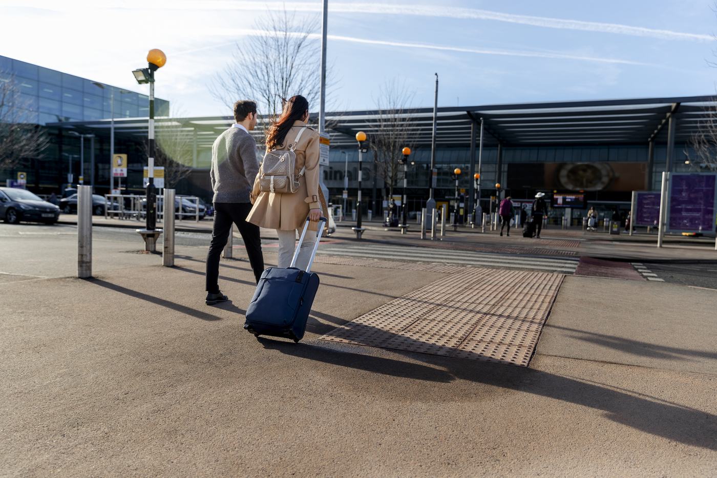 Two travellers walking to the terminal with their luggage